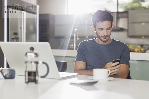 Mann texting mit Handy am Küchentisch