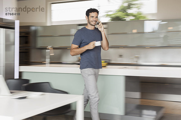 Lächelnder Mann beim Kaffeetrinken und Telefonieren in der Küche