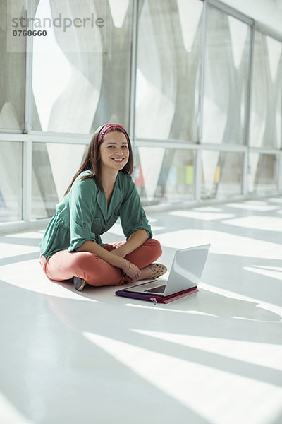 Porträt einer selbstbewussten Geschäftsfrau mit Laptop auf dem Boden im sonnigen Büro