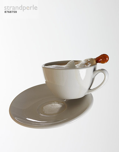 White coffee cup with white coffee and saucer falling in front of white background