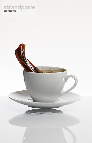 Schwarzer Kaffee spritzt aus weißer Kaffeetasse vor weißem Hintergrund