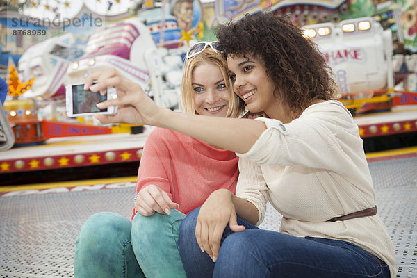 Two young women at the fairground photographing self