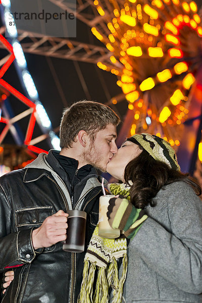 Deutschland  Berlin  glückliches junges Paar beim Küssen auf dem Weihnachtsmarkt vor dem beleuchteten Riesenrad