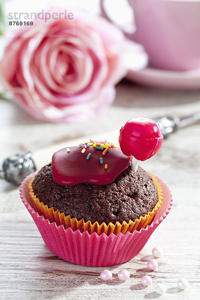 Schokoladenmuffin in Muffinpapier mit rotem Lolly und Zuckerguss auf gedeckter Tafel