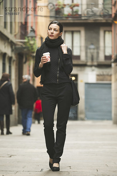 Spain  Catalunya  Barcelona  young black dressed businesswoman with coffee to go in front of a street