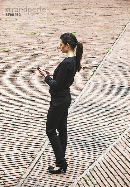 Spanien  Katalonien  Barcelona  junge schwarz gekleidete Geschäftsfrau mit Smartphone auf einem Platz stehend