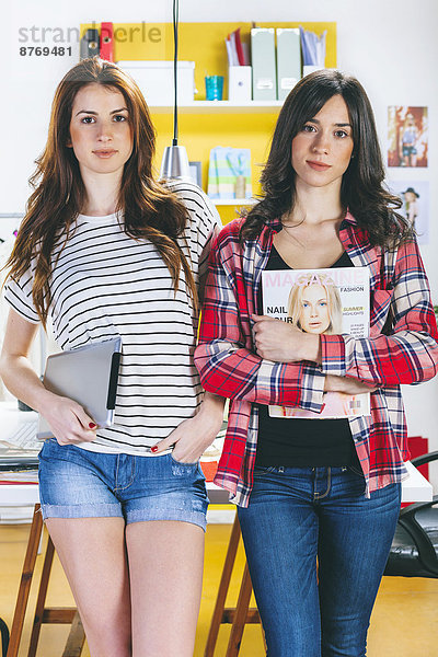 Portrait von zwei Modebloggerinnen mit digitalem Tablett und Magazin im Büro