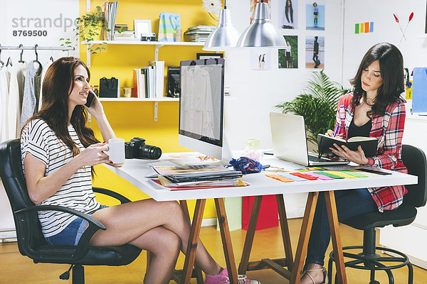 Two female fashion bloggers sitting at desk in the office