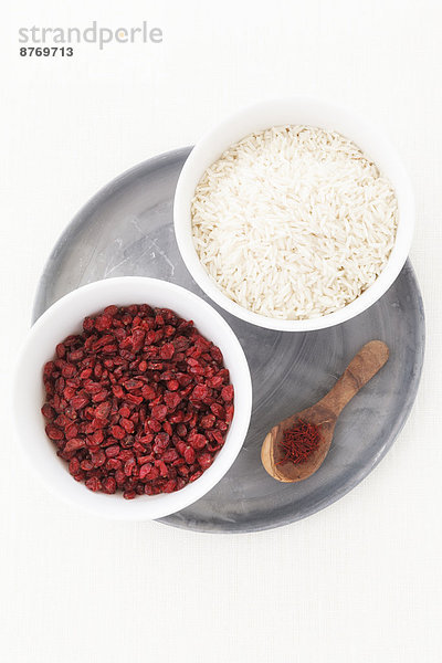 Bowls of barberries and rice  wooden spoon with saffron on dinner plate and white background