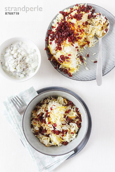 Persian saffron rice with barberries and bowl of mint yoghurt on white background