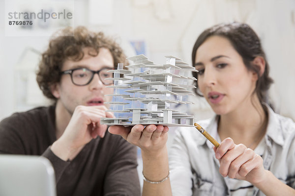Portrait of two young architects looking at architectural model in office