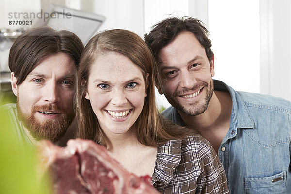 Porträt von drei Freunden in der Küche mit Steak