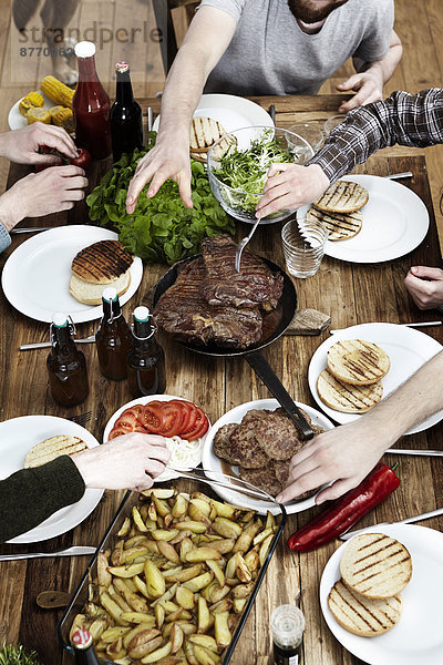 Freunde essen Kartoffeln  Steaks und Fleischbällchen an einem Holztisch.