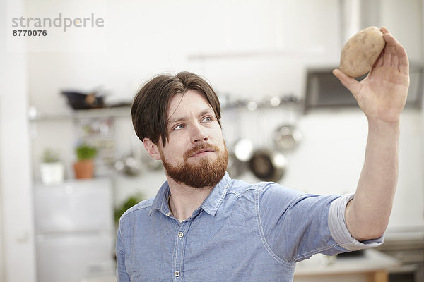 Mann in der Küche hält Kartoffel