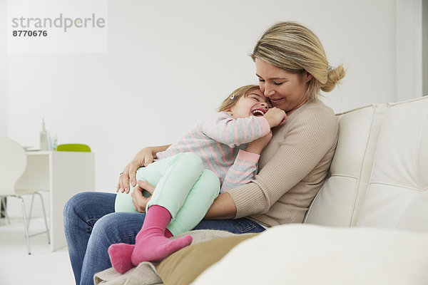 Deutschland  München  Mutter und Tochter auf Sofa sitzend  kuschelnd