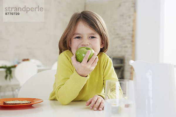 Mädchen am Tisch sitzend mit grünem Apfel