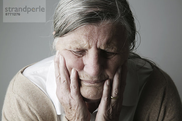 Porträt einer älteren Frau mit geschlossenen Augen und Kopf in den Händen