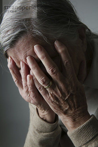 Seniorenfrau  die das Gesicht mit den Händen bedeckt.