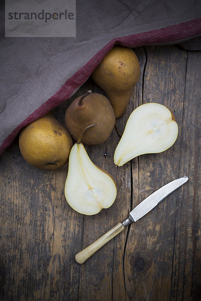 geschnittene und ganze Birnen (Pyrus)  ein Messer und ein Küchentuch auf Holztisch