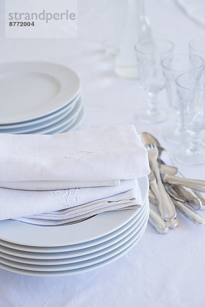 Gläser  Tellerstapel  Silberbesteck und Stoffservietten auf weißer Tischdecke