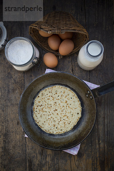 Pfannkuchen in der Pfanne und Zutaten  Eier  Milch und Mehl