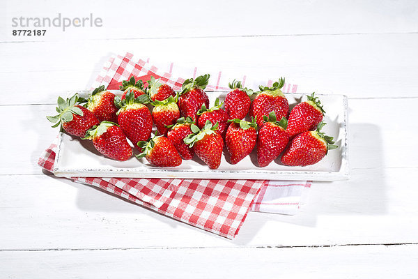 Erdbeerteller (Fragaria) auf Küchentuch und weißem Holztisch