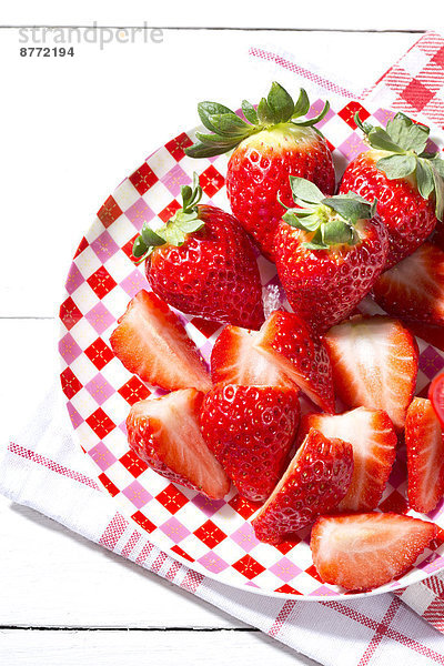 Teller mit geschnittenen und ganzen Erdbeeren (Fragaria) auf Küchentuch  Nahaufnahme