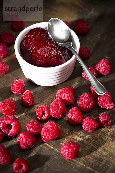 Bowl of raspberry jam  spoon and raspberries on wooden table