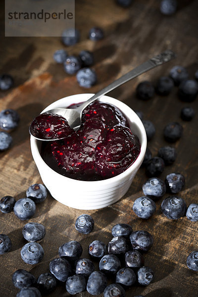 Bowl of blueberry and raspberry jam  spoon and blueberries on dark wooden table