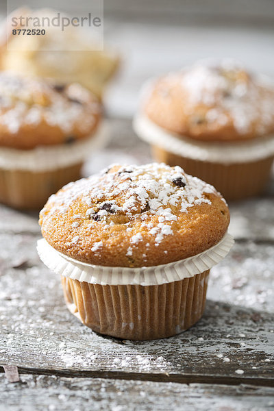 Muffins in paper cups sprinkled with powdered sugar on wooden table