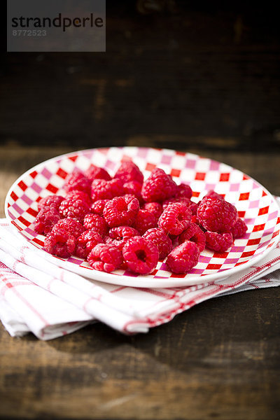 Dish of raspberries on kitchen towel and wooden table
