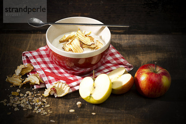 Bowl of lactose-free yogurt with dried apple rings and and apples on wooden table