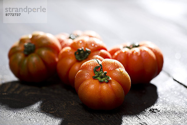 Five oxheart tomatoes on dark wood  close-up