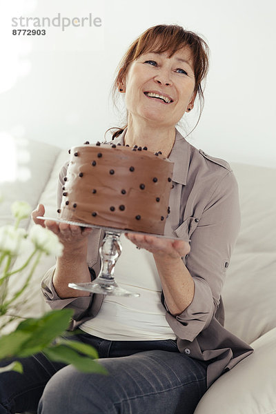 Portrait of smiling woman holding cake stand with chocolate cake