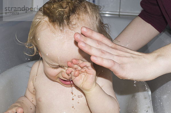 Kleinkind in der Badewanne wird von Mutter gewaschen