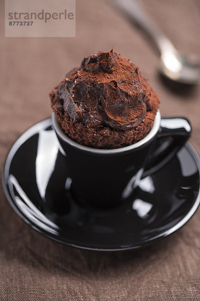Schwarze Tasse Schokoladenkuchen und ein Teelöffel auf braunem Tuch