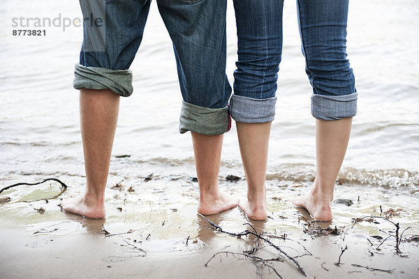 Nackte Füße eines jungen Paares  das im Wasser des Rheins steht.