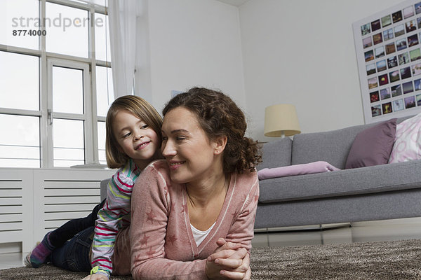 Happy mother and daughter lying on carpet in living room