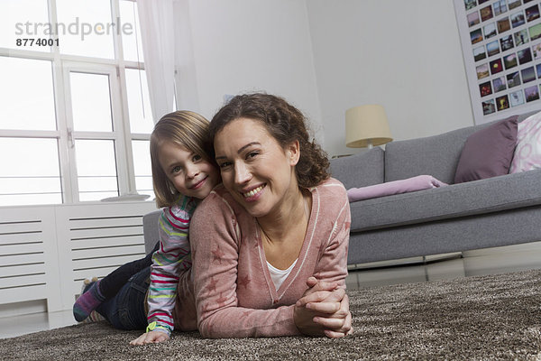 Glückliche Mutter und Tochter auf Teppich im Wohnzimmer liegend