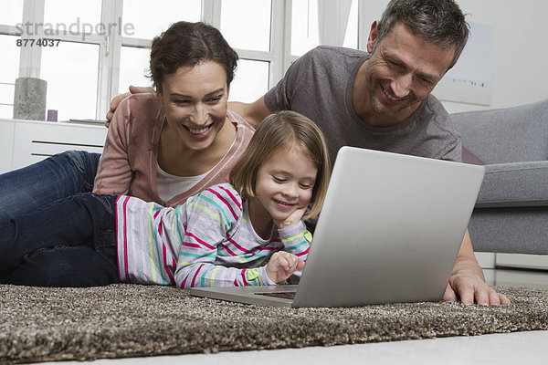 Father  mother and daughter using laptop on carpet in living room