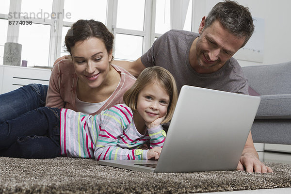 Vater  Mutter und Tochter mit Laptop auf Teppich im Wohnzimmer