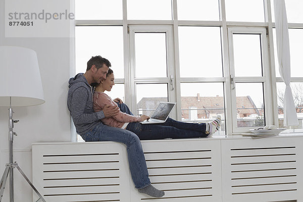Couple sitting on windowsill using laptop