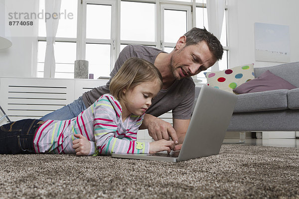 Father and daughter using laptop on carpet in living room