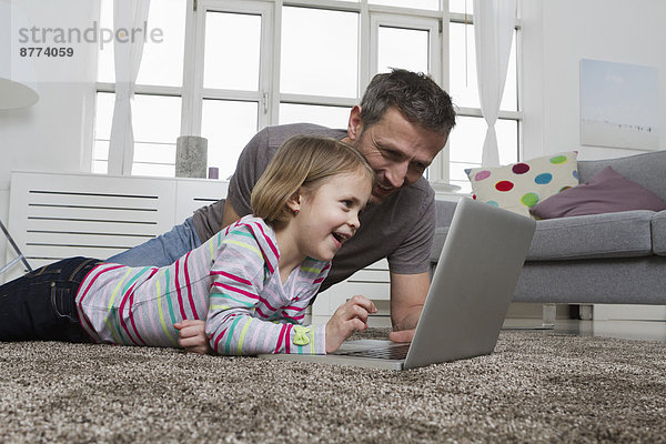 Vater und Tochter mit Laptop auf Teppich im Wohnzimmer