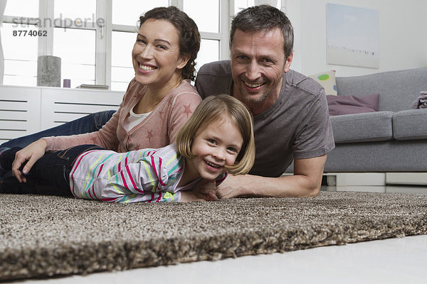 Happy mother  father and daughter lying on carpet in living room