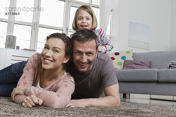 Happy mother  father and daughter lying on carpet in living room