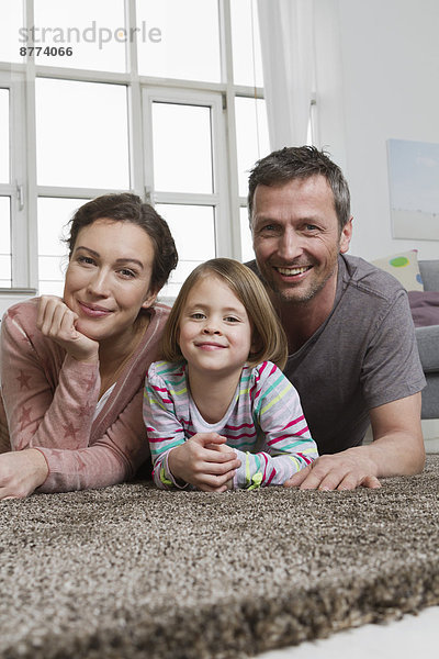 Glückliche Mutter  Vater und Tochter auf Teppich im Wohnzimmer liegend