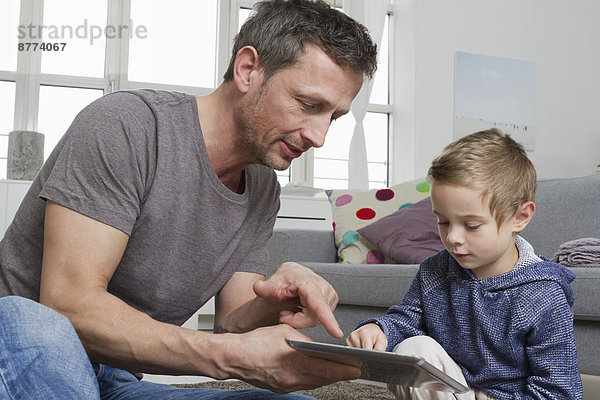 Father and son using tablet computer in living room