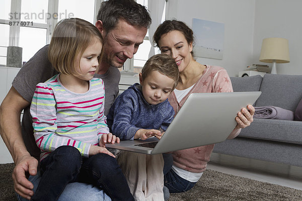 Glückliche vierköpfige Familie mit Laptop im Wohnzimmer