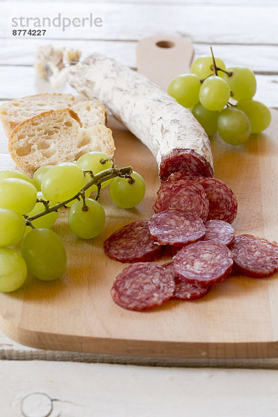 Chopped salami  green grapes  tomatoes and baguette on chopping board
